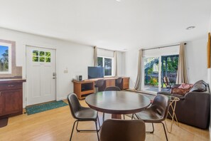 Ein modernes Wohnzimmer mit Esstisch, Stühlen, einer Couch, einem Fernseher und einer Glastür, die auf einen Balkon führt.