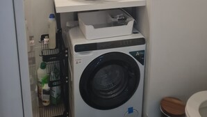 Un baño pequeño con lavamanos blanco, un espejo encima, lavadora y retrete.