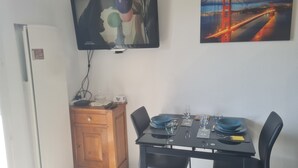 Un comedor con una mesa dispuesta para dos personas, un televisor montado en la pared y un cuadro del Puente Golden Gate.