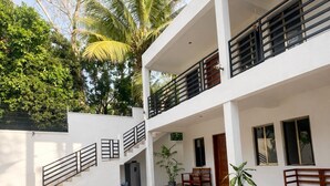 Un edificio de dos pisos con un patio cubierto, asientos al aire libre y una palmera.