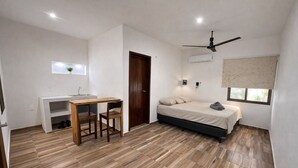 Una habitación compacta con cama, escritorio, silla, ventilador de techo y ventana.