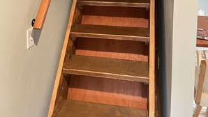 Eine Holztreppe mit Handlauf, die zu einem Raum mit heller Wand und einer Tür oben führt.