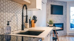 A modern kitchen with a hexagonal tile backsplash, a black faucet, and a glass countertop. - LAO LOFT 105 by Gestion ELITE (Mont-Tremblant)