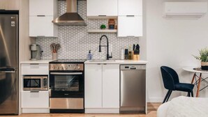 A modern kitchen with white cabinets, a stainless steel refrigerator, a built-in oven, a dishwasher, and a microwave. - LAO LOFT 105 by Gestion ELITE (Mont-Tremblant)