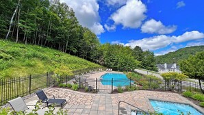 A swimming pool with a stone patio, lounge chairs, and a fence. - LAO LOFT 105 by Gestion ELITE (Mont-Tremblant)