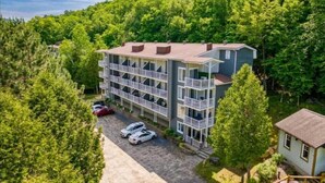 A multi-story building with balconies, surrounded by dense forest, and a parking area with cars. - LAO LOFT 105 by Gestion ELITE (Mont-Tremblant)
