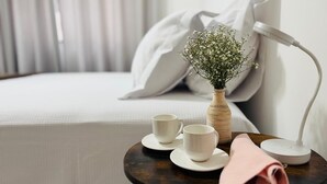 A neatly arranged hotel room with a bed, a bedside table with a lamp, a vase with flowers, and two cups on the table.
