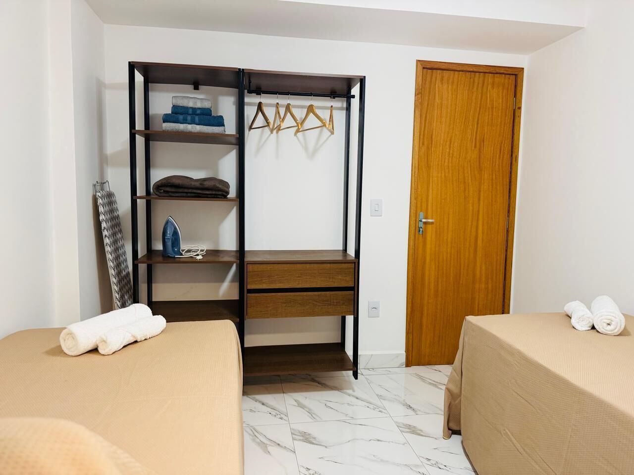 A room with a wardrobe, two beds, a wooden door, and a small ironing board.