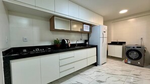 A kitchen with white cabinets, a black countertop, a microwave, a coffee maker, and a washing machine.