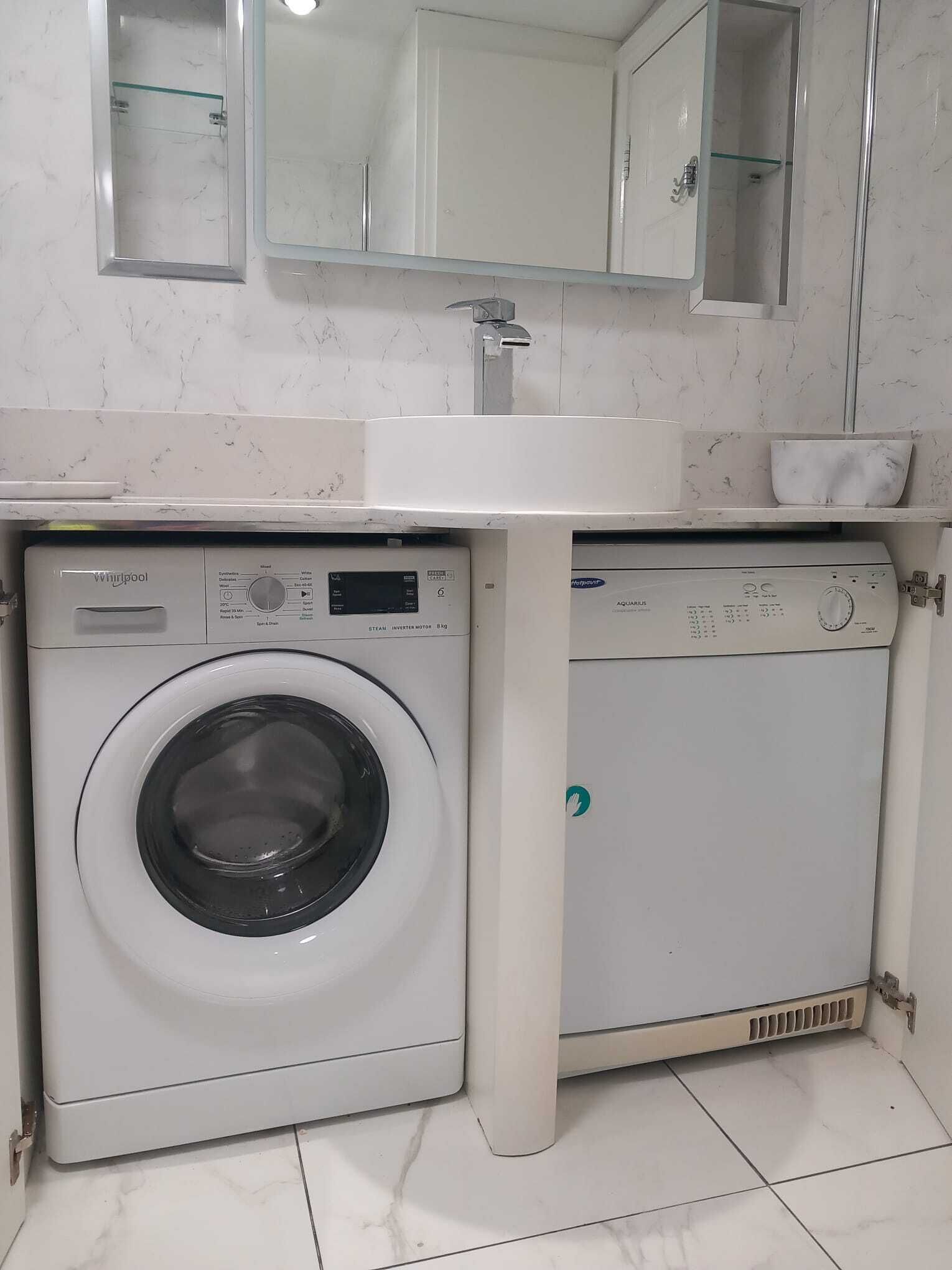 A compact laundry area with a front-loading washer and a top-loading dryer, a sink, and a mirror above the sink.