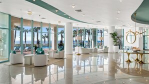 Eine großzügige Lobby mit modernem Design, inklusive einer geräumigen Sitzecke mit weißen Sofas und einem goldenen Tisch.