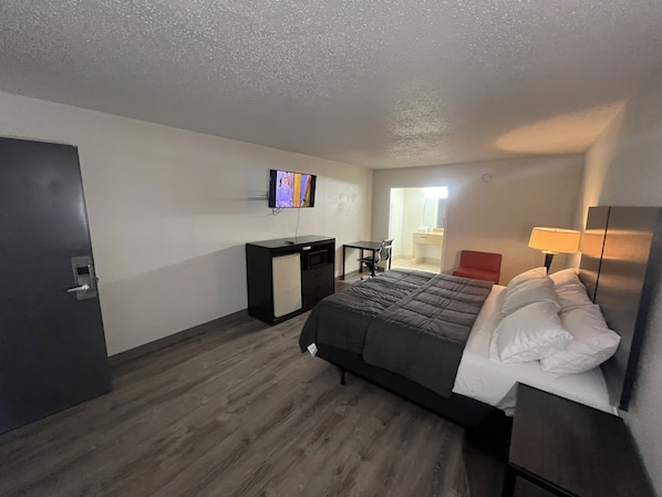 A hotel room with a bed, desk, chair, TV, and a bathroom visible through an open door. - Skylite inn (Austin)