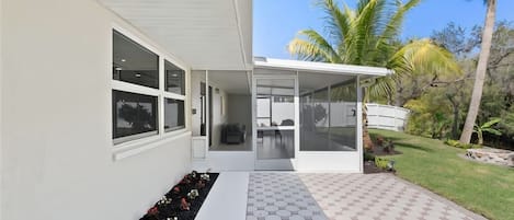 A modern house with large windows, a covered patio, and a well-maintained garden with palm trees.