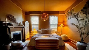 Ein gemütliches Schlafzimmer mit Kamin, großem Fenster, einer Pendelleuchte und einem Blumentopf.