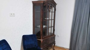 Quarto com um armário de madeira, duas cadeiras azuis, piso de madeira e cortina cinza.