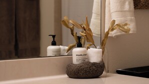 Un meuble-lavabo de salle de bain avec un miroir, un porte-serviettes, une bouteille de lotion pour le corps et des fleurs séchées dans un vase en verre.