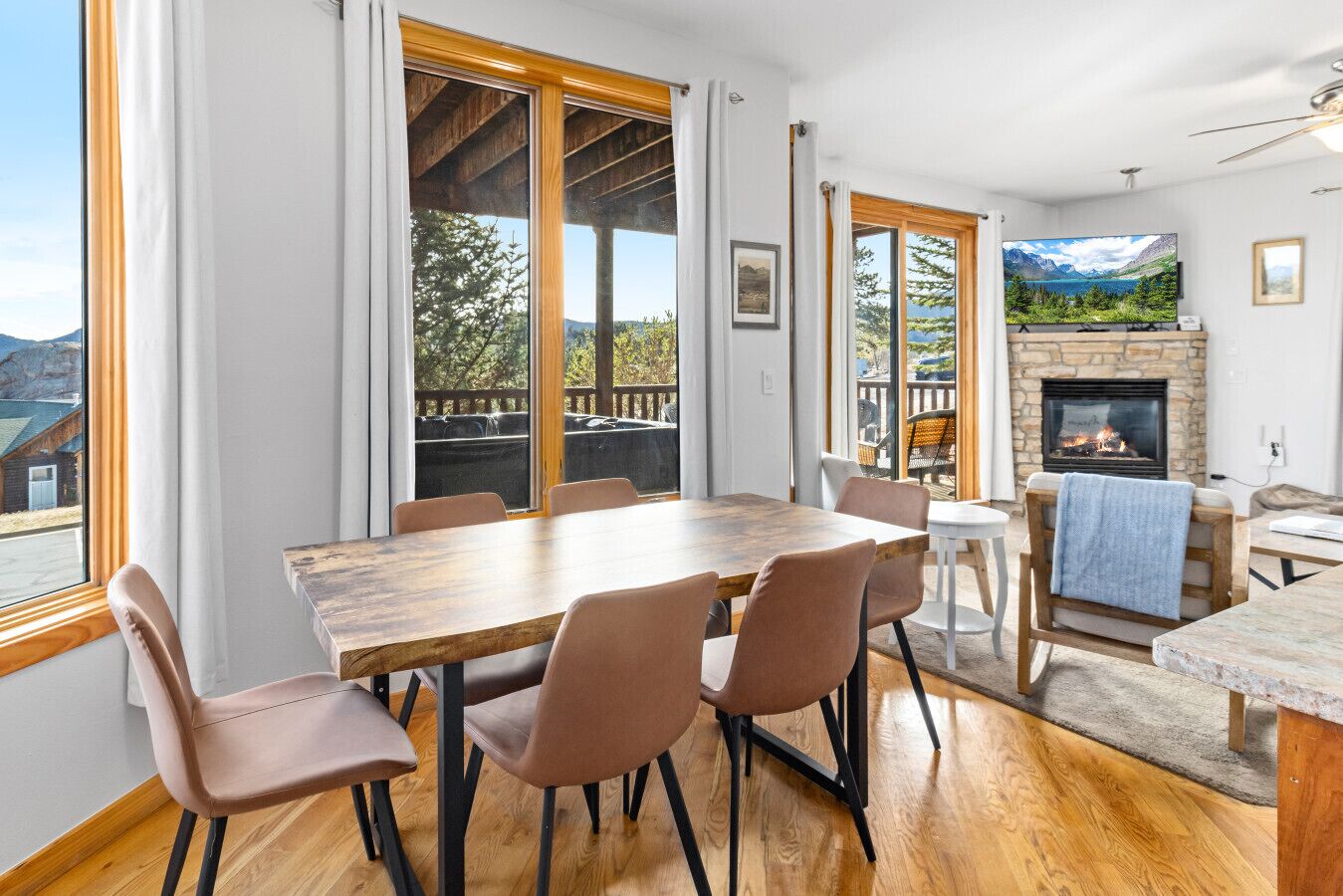 A dining area with a wooden table and chairs, a fireplace, and large windows with a view of the outdoors.
