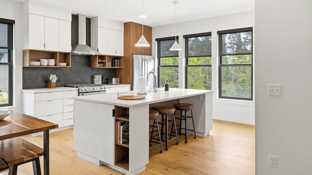 A modern kitchen with white cabinetry, a central island with stools, a stove, and a large window providing a view of greenery.