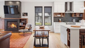 A modern kitchen with a fireplace, a dining area, and a large TV mounted on the wall.