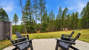Two Adirondack chairs on a concrete patio with a view of a forest and a shed.