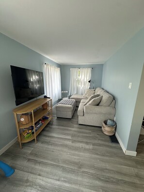 Sala de estar con televisor de pantalla plana, sofá, mesa de centro y estante de madera con cestas de almacenamiento.
