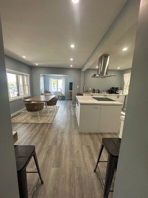 A modern kitchen with white cabinetry, a stainless steel range hood, and a dining area with a table and chairs.