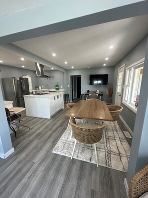 Una cocina moderna con una isla central, electrodomésticos integrados y un comedor con una gran mesa de madera y sillas de mimbre.