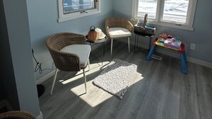 Una habitación con dos sillones de mimbre, una mesita con juguetes y una ventana con vistas a un paisaje nevado.