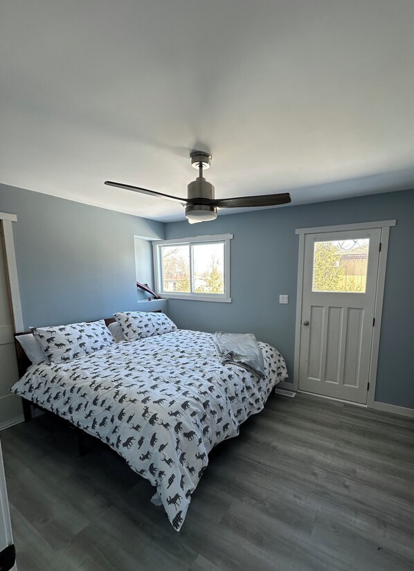 A bedroom with a bed, a ceiling fan, two windows, and a door.