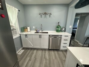 A kitchen with white cabinets, a stainless steel dishwasher, a sink with a faucet, and a green water bottle on the counter.