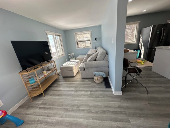 A compact living space with a sofa, a television, a small table, and a kitchen area.