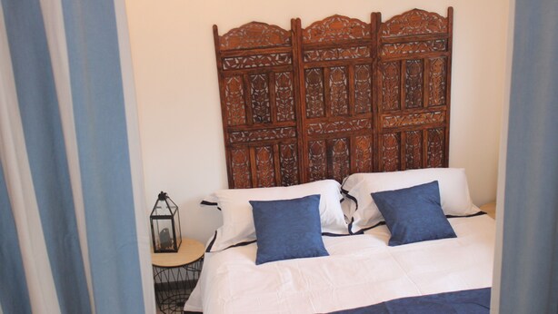 A bedroom with a wooden headboard, a bed with white and blue bedding, and a small table with a lantern. - Two-room apartment (Castelnau-Rivière-Basse)
