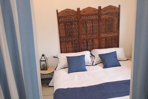 A bedroom with a wooden headboard, a bed with white and blue bedding, and a small table with a lantern. - Two-room apartment (Castelnau-Rivière-Basse)