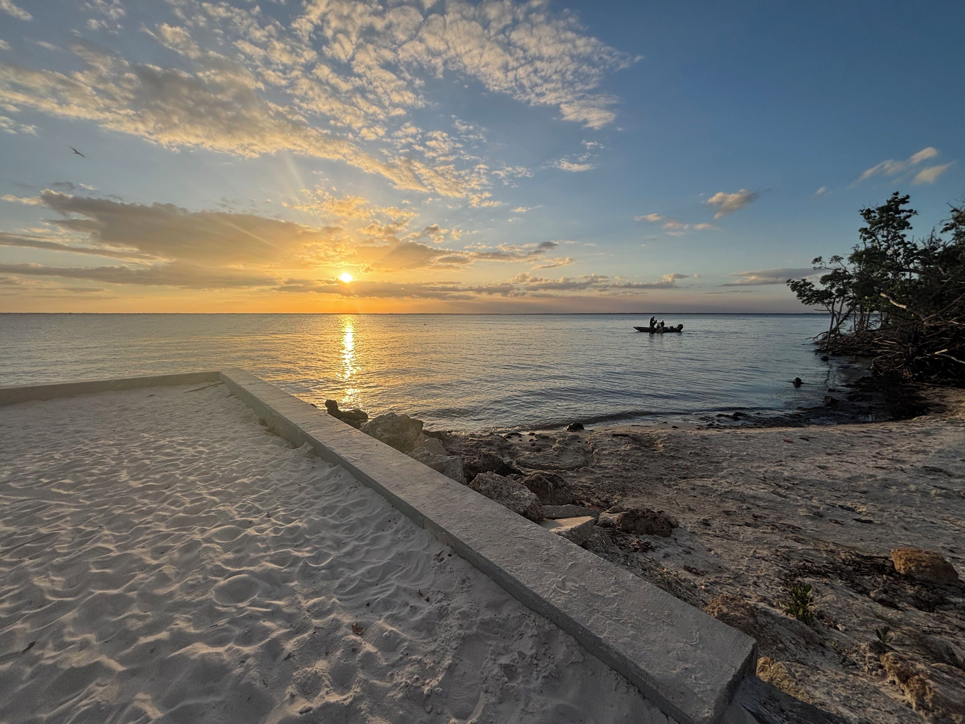 A beach with a concrete walkway, calm sea, and a boat in the distance.