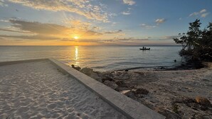 En strand med en betonpromenade, rolig sø og en båd i det fjerne.