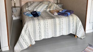 Et soveværelse med sengegavl i træ, en seng med et mønstret sengetæppe, et natbord med lampe og et lille bord med lampe.