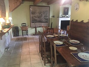 A dining area with a wooden table set for four, chairs, a fireplace, and a painting on the wall. - An authentic, peaceful retreat with a fenced-in wooded lot in the city center (Sainte-Marie-de-Ré)