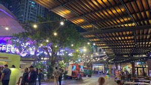 An outdoor cafe area with tables and chairs, surrounded by trees and string lights. - Spectacular 2.5BR Connected to Eastwood  Mall (Quezon City)
