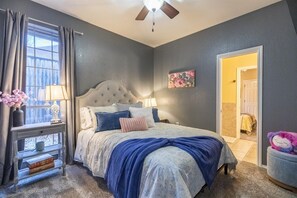 Une chambre à coucher avec un lit, des tables de chevet, un ventilateur de plafond et une fenêtre avec des rideaux.