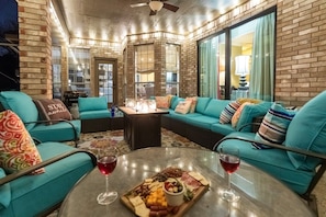 Un espacio interior acogedor con sofás color turquesa, una mesa de vidrio con una tabla de embutidos y copas de vino, y paredes de ladrillo.