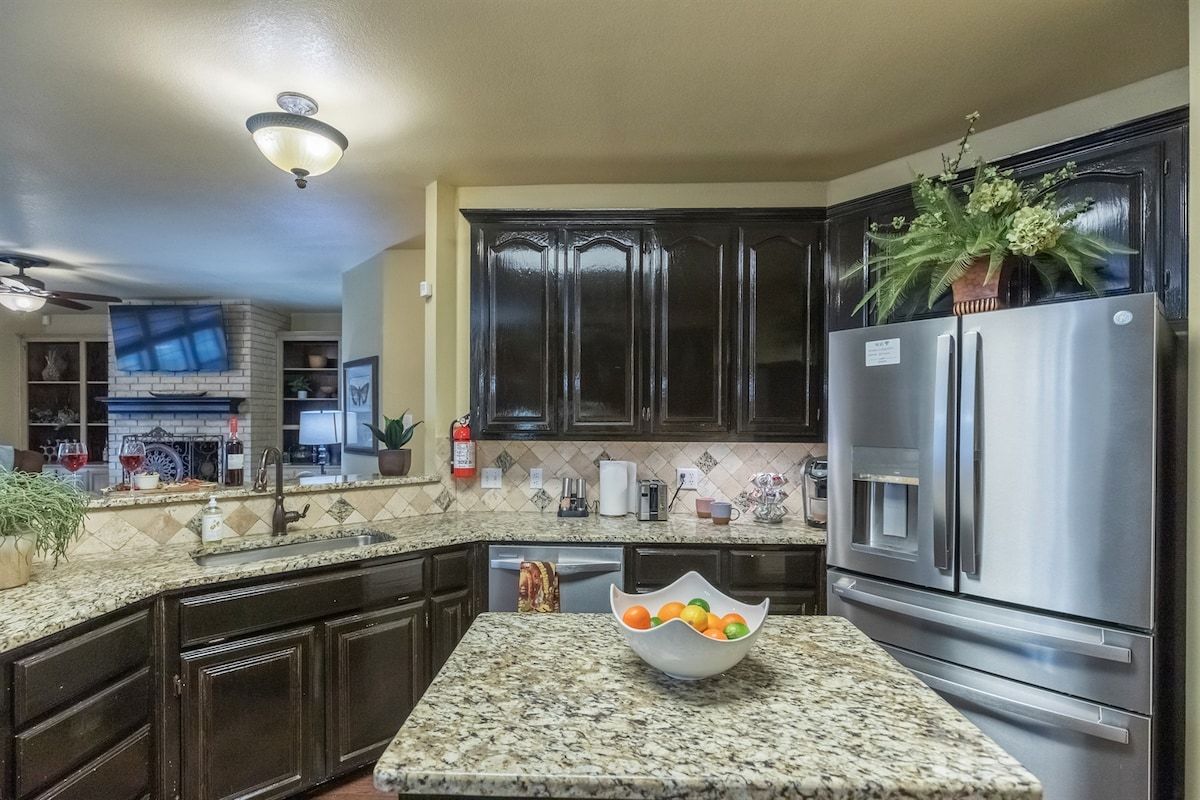 A kitchen with dark cabinets, a stainless steel refrigerator, a granite countertop, and a bowl of fruit.