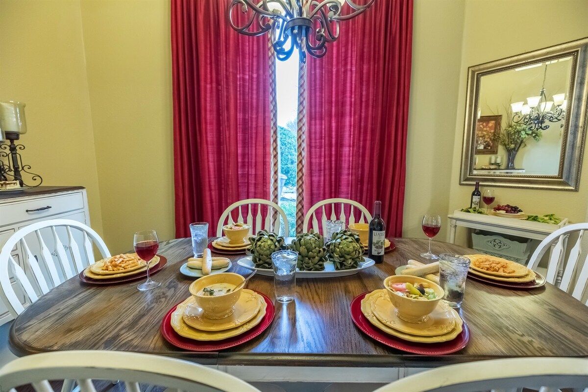 Een eettafel gedekt voor vier personen, met rood en goud servies, een kroonluchter en een spiegel aan de muur.