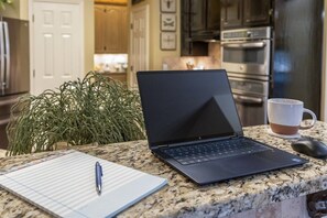 A laptop on a kitchen counter with a notebook and pen beside it.