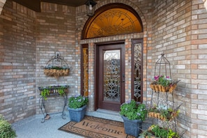 Una entrada de ladrillo con felpudo, plantas en macetas y cestas metálicas decorativas.