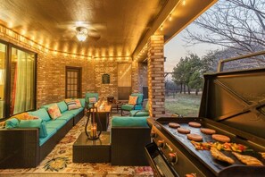 Une terrasse extérieure avec un mur en briques, des meubles de jardin verts, un barbecue et une vue sur les arbres.