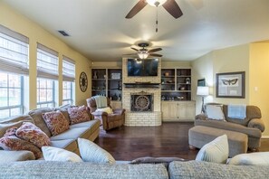 A living room with a fireplace, a ceiling fan, and a television.