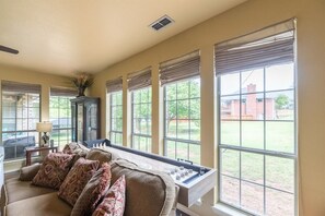 A living room with a sofa, a coffee table, and a view of a brick building through large windows. - The Regent Abilene Luxury Retreat w Patio Fire (Abilene)