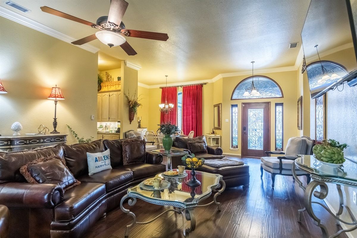Un salon doté d’un ventilateur de plafond, d’une table basse agrémentée d’objets décoratifs, d’un canapé et d’un coin repas avec une table en verre.