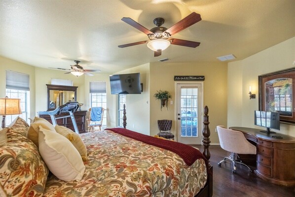 A bedroom with a bed, a desk, a chair, a ceiling fan, and a television.