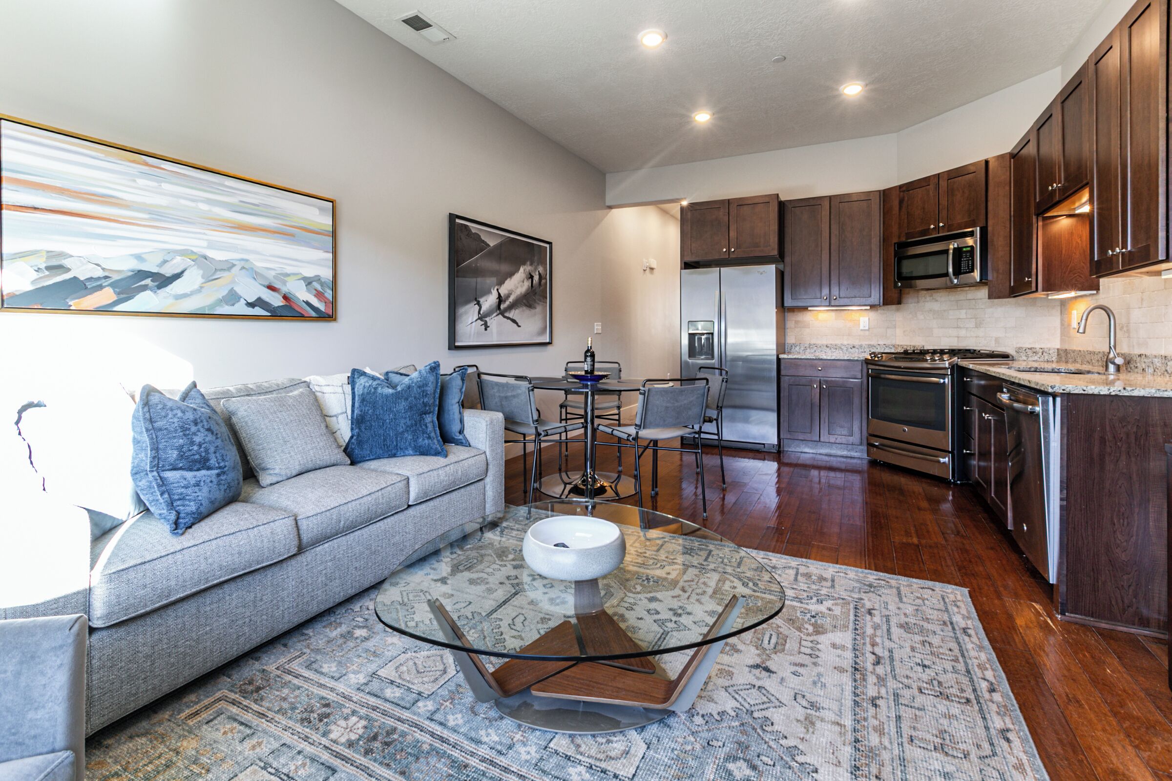 A modern kitchen with dark wood cabinets, stainless steel appliances, and a glass-top coffee table.